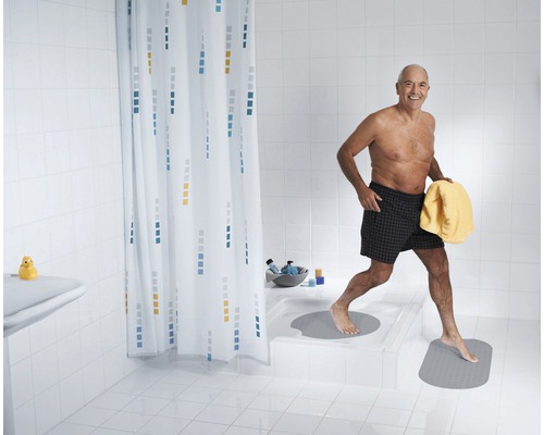Badezimmer mit Duschvorhang und Badematten, eine Person verlässt die Dusche