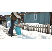Eine Person schippt Schnee mit einer Schneeschaufel vor einem Haus.