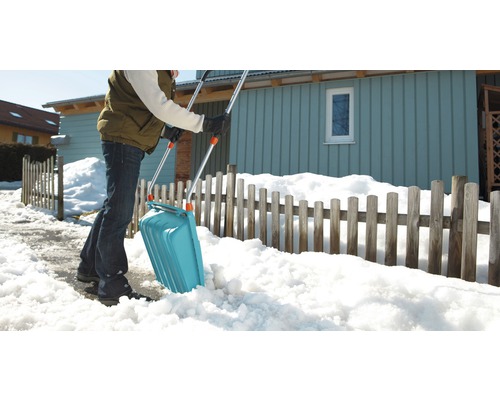 Eine Person schippt Schnee mit einer Schneeschaufel vor einem Haus.