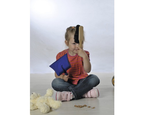 Ein Mädchen sitzt auf dem Boden und spielt mit einer Kehrschaufel und einem Handfeger.