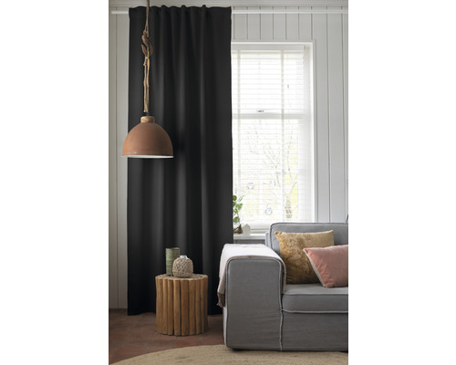 Wohnzimmer mit Sofa, Beistelltisch aus Holz, Lampe und schwarzem Vorhang.