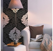 Wohnzimmer mit Ornamenttapete, Stehlampe, Sessel, Kissen, Decke, Buch und Beistelltisch