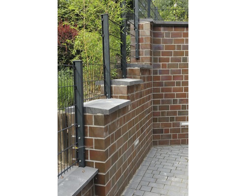 Gartenzaun aus Metall neben einer Ziegelmauer mit Steinabdeckung