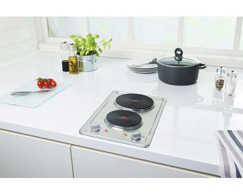 Küchenszene mit Doppelkochplatte, Topf, Geschirr, Gewürzen und Lebensmitteln auf einer hellen Arbeitsfläche