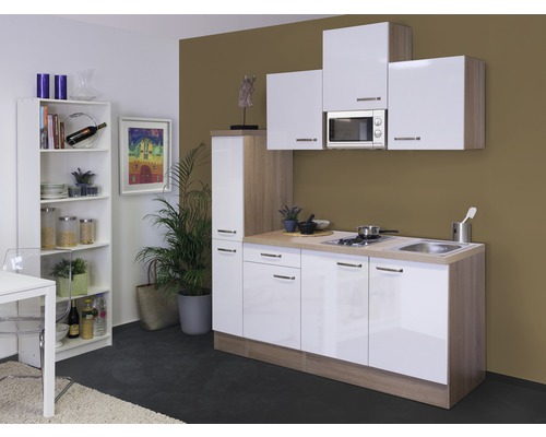 Singleküche Flex Well Valero 9876 weiß/Sonoma Eiche 180 cm inkl. Einbaugeräte Küchenzeile mit Spüle, Kochfeld, Mikrowelle und Hochschrank neben einem Bücherregal.