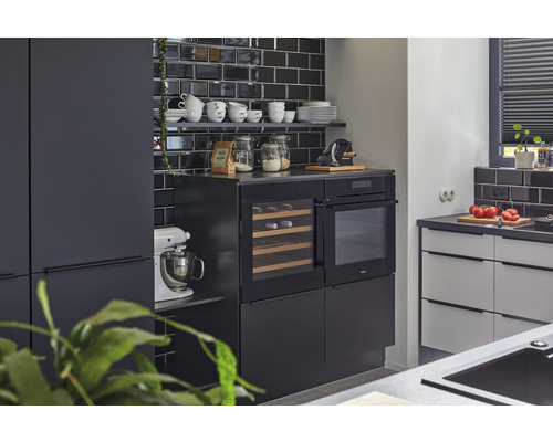 Moderne Küche mit schwarzen Fliesen, Einbaugeräten und Küchenutensilien auf Regalen.