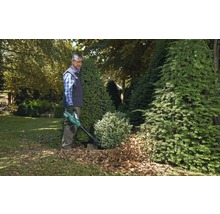 Ein Mann benutzt einen Laubbläser im Garten, um Laub zu entfernen.