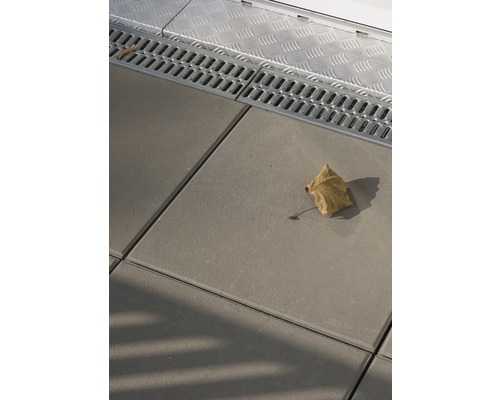 Drainagerinne neben Betonpflastersteinen und einem Blatt