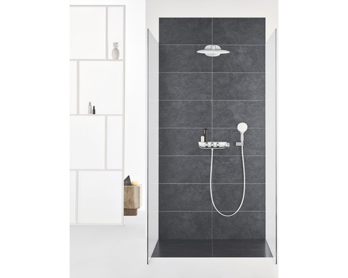 Moderne Dusche mit Kopfbrause, Handbrause und Ablage vor dunklem Fliesenhintergrund.