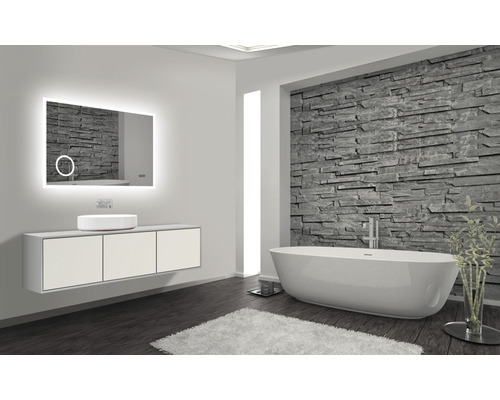 Badezimmer mit beleuchtetem Spiegel, Waschtisch, Aufsatzwaschbecken und Badewanne vor Steinwand