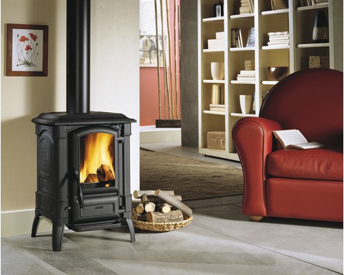 Gusseisenofen mit brennendem Holz in einem Wohnzimmer mit Sessel und Bücherregal