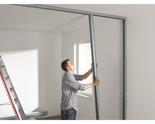 Mann montiert Trockenbauwand mit Metallprofilen in einem Raum.