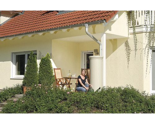 Haus mit Regenwassertank, Terrasse und Frau mit Gießkanne