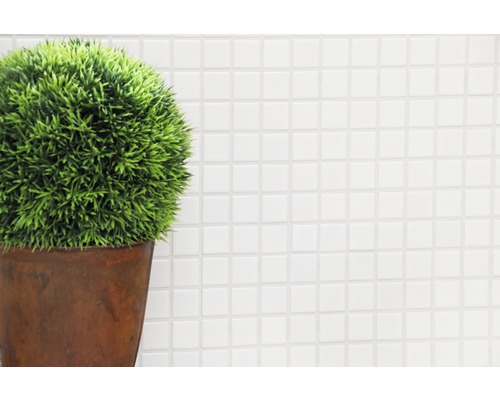 Dekorative Kunstpflanze in einem Topf vor einem weißen Mosaikhintergrund