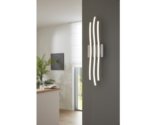 Moderne Wandleuchte mit drei geschwungenen Leuchtelementen an einer grauen Wand
