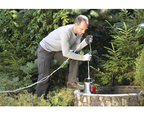 Ein Mann lässt eine Tiefbrunnenpumpe in einen Brunnen hinab