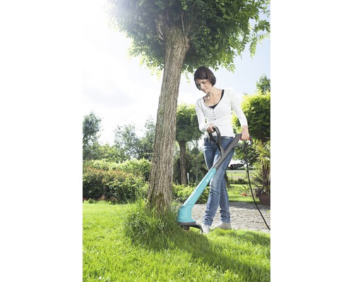 Frau benutzt einen Rasentrimmer im Garten, um Gras zu schneiden.