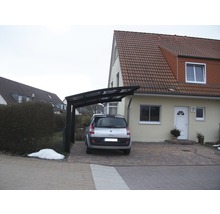 Ein Carport aus Metall vor einem Wohnhaus mit gepflasterter Auffahrt und einem geparkten Auto.