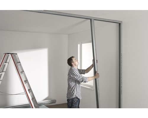 Mann montiert Metallprofile für Trockenbauwand in einem Raum.
