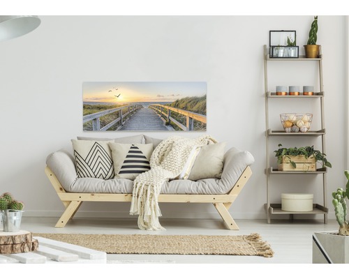 Wohnzimmer mit Sofa, Regal und einem Wandbild mit einem Weg zum Strand bei Sonnenuntergang