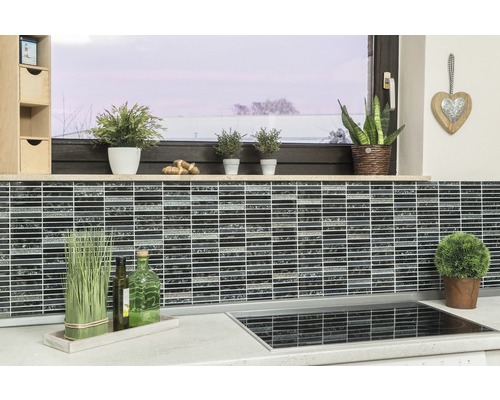 Küchenszene mit Mosaikfliesen an der Wand, Pflanzen und Küchenutensilien auf der Arbeitsfläche.