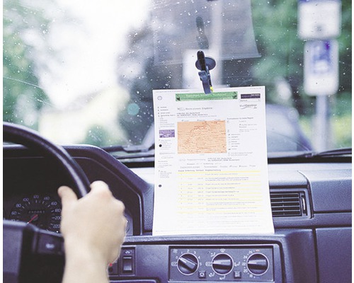Ein Blatt Papier mit Informationen, befestigt mit einem Saugnapfhalter an der Windschutzscheibe eines Autos.
