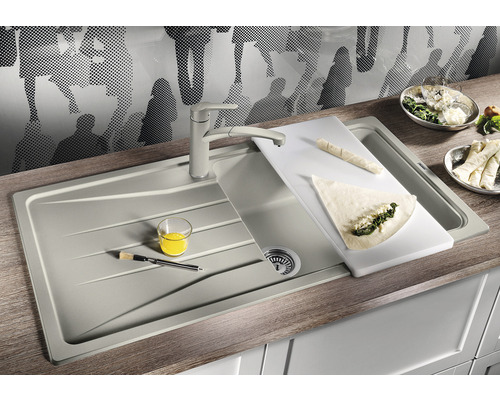 Küchenspüle mit Schneidebrett, Armatur, Speisen und Küchenutensilien auf einer Arbeitsplatte