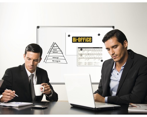 Zwei Männer sitzen an einem Tisch mit Laptop vor einer Whiteboard-Präsentation im Büro.