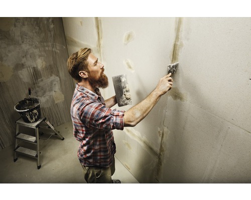 Mann verspachtelt Wand mit Spachtelmasse und Werkzeug