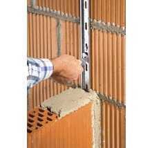 Handwerker befestigt eine Metallschiene an einer Ziegelwand mit Mörtel.