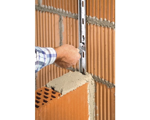 Handwerker befestigt eine Metallschiene an einer Ziegelwand mit Mörtel.