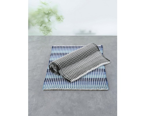 Zwei Badteppiche, einer blau gestreift und einer schwarz-weiß gemustert, liegen auf einem Untergrund.