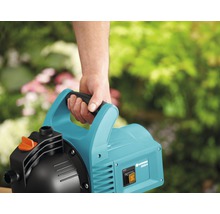 Gardena Hauswasserwerk 3000/4 mit Tragegriff in der Hand vor Gartenkulisse