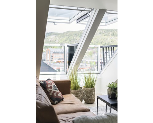 Helles Dachzimmer mit braunem Sofa, Zimmerpflanzen und Dachfenstern.