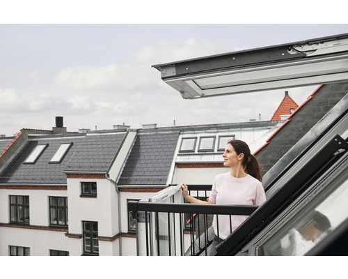 Frau auf einem Dachbalkon mit geöffnetem Dachfenster und Ausblick auf die Stadt