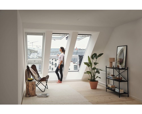 Helles Dachzimmer mit Dachfenstern, Frau, Sessel und Zimmerpflanze