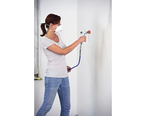 Frau mit Atemschutzmaske und Farbspritzpistole beim Malen einer Wand