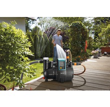 Garten mit Hauswasserwerk und Person, die mit einem Schlauch gießt