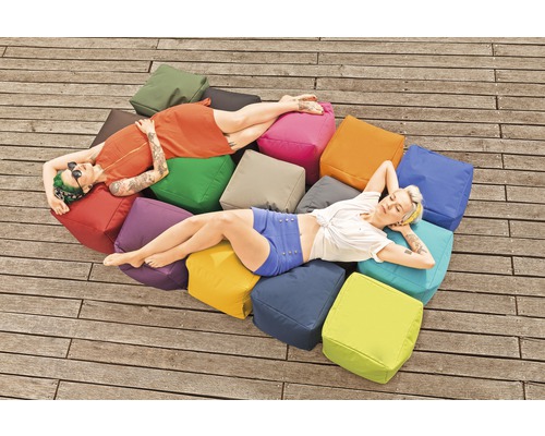 Zwei Frauen entspannen auf einem Haufen quadratischer Sitzkissen im Freien.