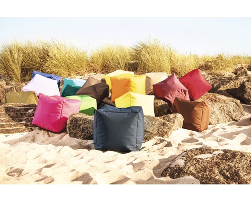 Eine Ansammlung von quadratischen Sitzkissen unterschiedlicher Farben auf Sand und Felsen.
