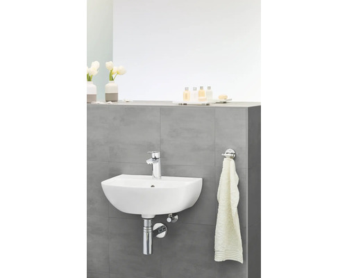 Hängewaschbecken im Badezimmer mit Armatur, Handtuch und Badezimmerutensilien