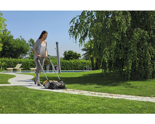 Frau benutzt eine Kehrmaschine zur Reinigung eines Gartenwegs.