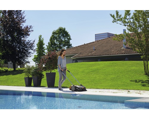 Eine Frau benutzt einen Rasenkehrer am Poolrand in einem Garten.
