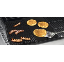 Grill mit Würstchen und Pfannkuchen auf einer Grillplatte mit einem Pfannenwender