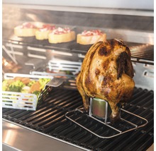 Gegrilltes Hähnchen auf einem Getränkehalter mit Gemüse und Brotscheiben im Hintergrund.