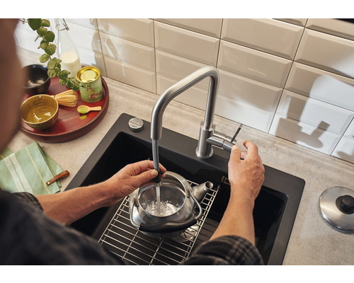 Person befüllt Teekessel in Spüle mit Wasserhahn