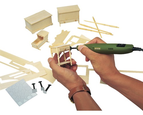 Person bearbeitet Miniaturmöbel mit einer Schleifmaschine. Im Hintergrund sind weitere Miniaturmöbel und Werkzeuge zu sehen.