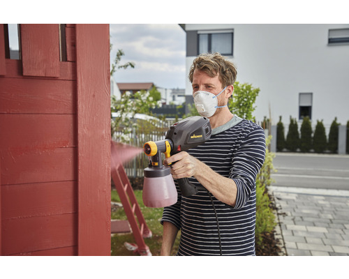 Mann streicht Holz mit Farbsprühsystem und Atemschutzmaske