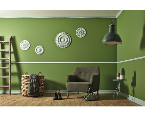 Wohnzimmer mit Sessel, Lampe, Leiter und Dekorationsartikeln vor grüner Wand