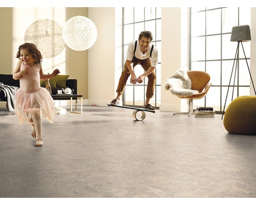 Helles Wohnzimmer mit Bodenbelag, in dem ein Mann auf einem Balance Board steht und ein Kind herumläuft